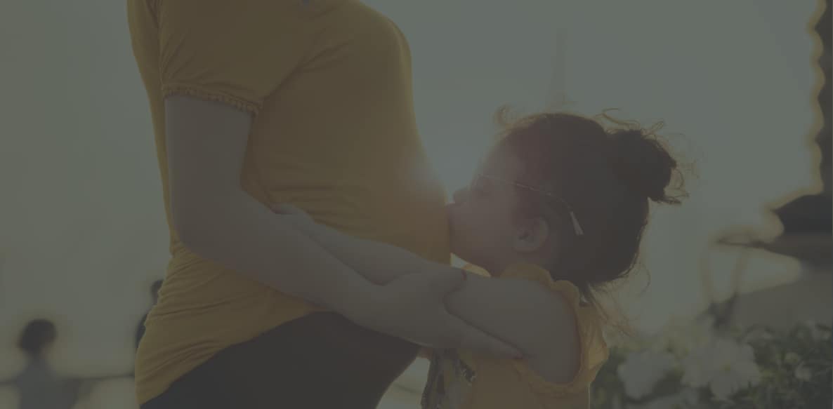 Child kissing woman's pregnant belly